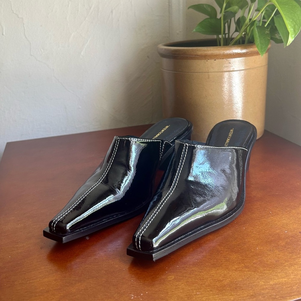 Intentionally Blank black patent pointed-toe mule with contrast stitching.